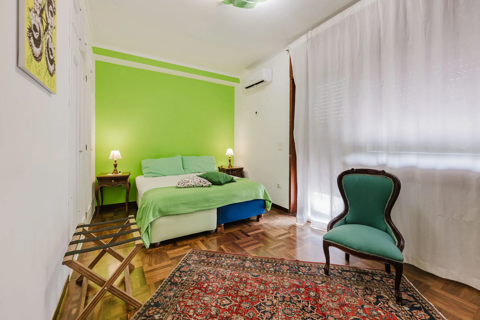 Camera con parete verde, letto matrimoniale, tappeto persiano e poltrona