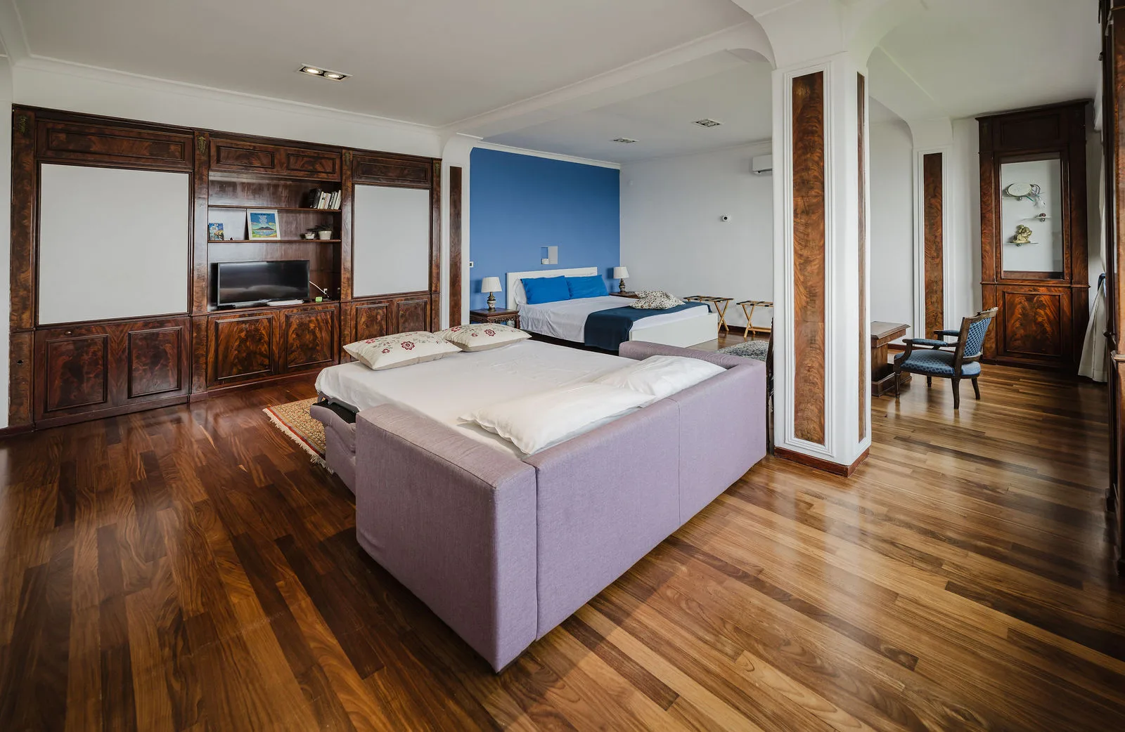 Camera con parete azzurra, letto matrimoniale, divano e boiserie in legno